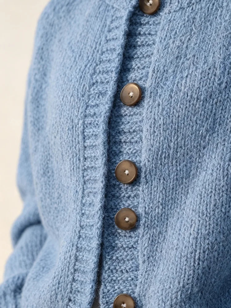 The women's smog-blue solid-color knitted cardigan is made of thick knitted fabric. It has a round neck and front buttons. It is suitable for wearing in autumn and winter, has strong versatility, and has a slightly European-s